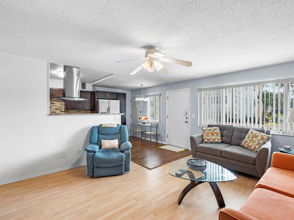 A living room features light wood flooring, a blue entertainment center, and an orange sofa — 1235 S HIGHLAND AVENUE UNIT 2-207, CLEARWATER, FL
