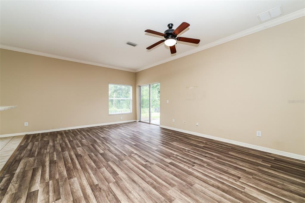 An empty living room features wood-look flooring, a ceiling fan, and a sliding glass door — 14831 HERONGLEN DRIVE, LITHIA, FL