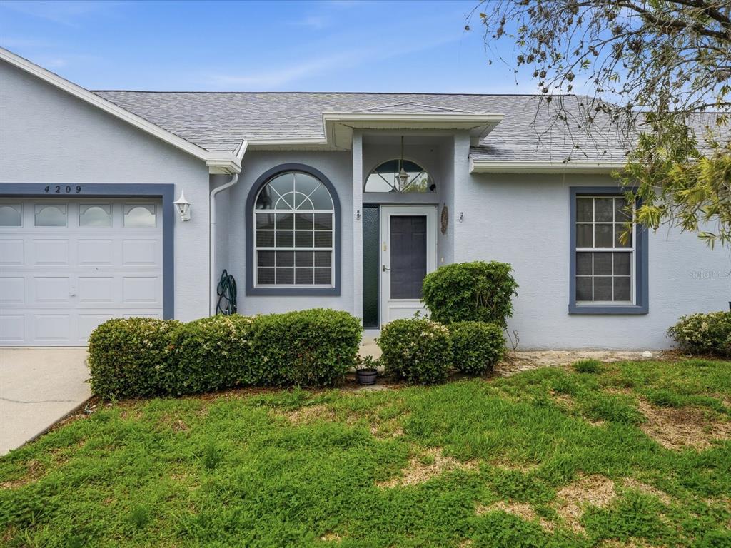 The exterior of a light blue house features a garage, arched window, and front entrance — 4209 AVANTI CIRCLE, NEW PORT RICHEY, FL