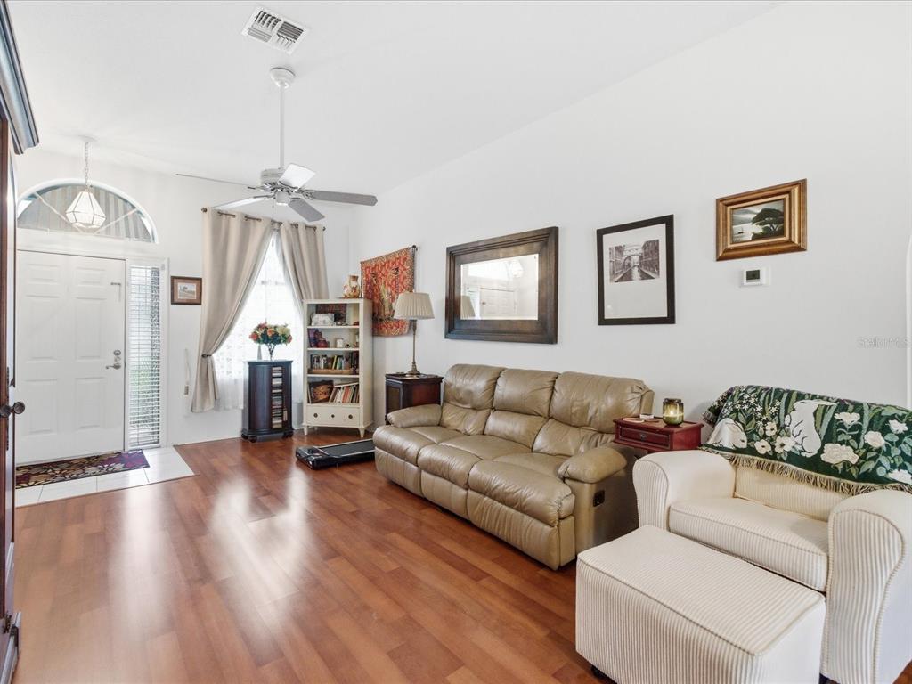 A living room features wood flooring, a tan leather sofa, and a white front door — 4209 AVANTI CIRCLE, NEW PORT RICHEY, FL