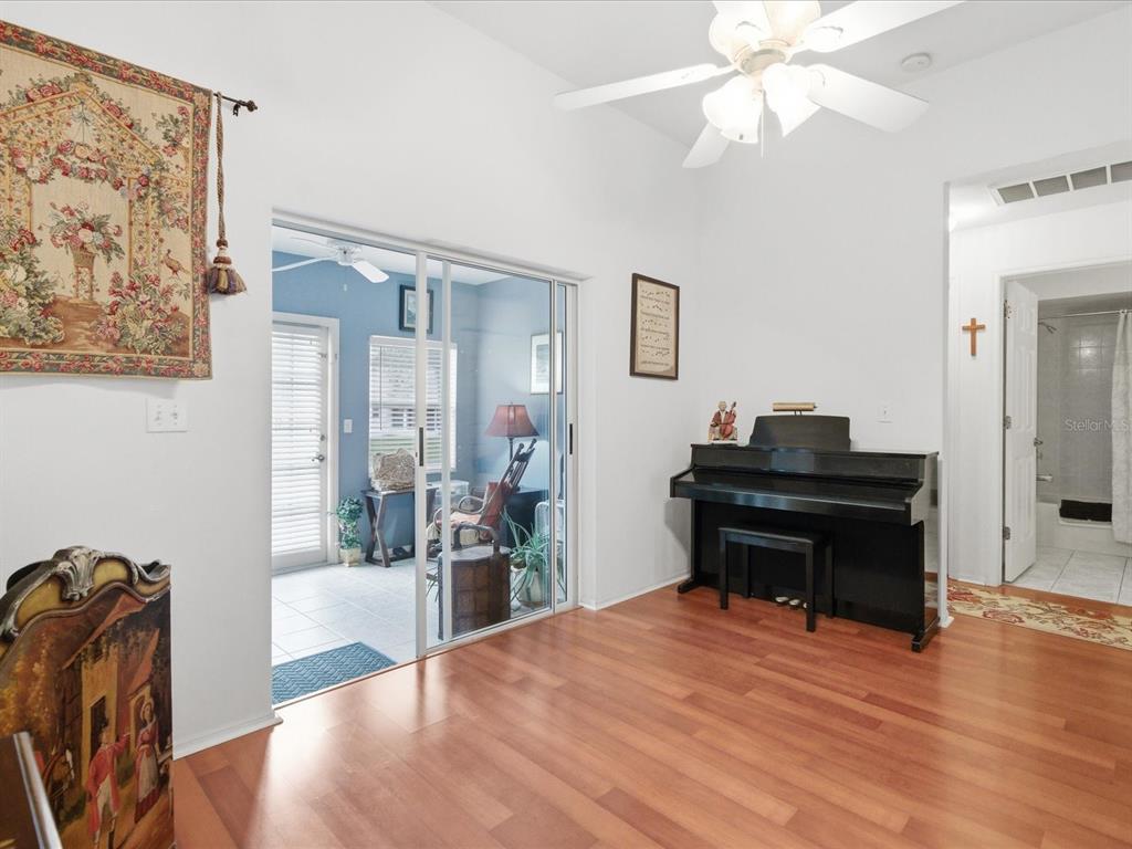 A room with wood flooring, a black piano, and sliding glass doors to a sunroom — 4209 AVANTI CIRCLE, NEW PORT RICHEY, FL