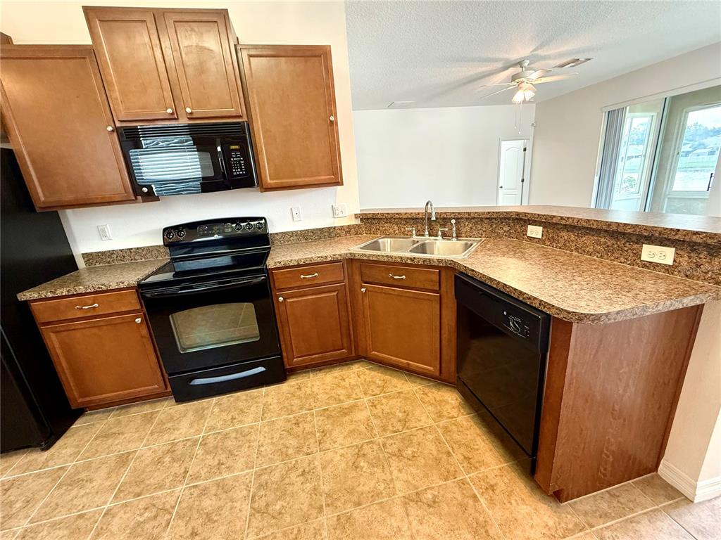 A kitchen features wood cabinets, black appliances, a corner sink, and tan tile flooring — 2616 WALDEN WOODS DRIVE, PLANT CITY, FL