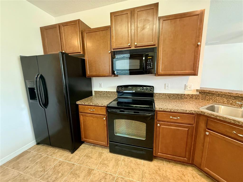 A kitchen features brown wooden cabinets, black appliances, and granite countertops — 2616 WALDEN WOODS DRIVE, PLANT CITY, FL