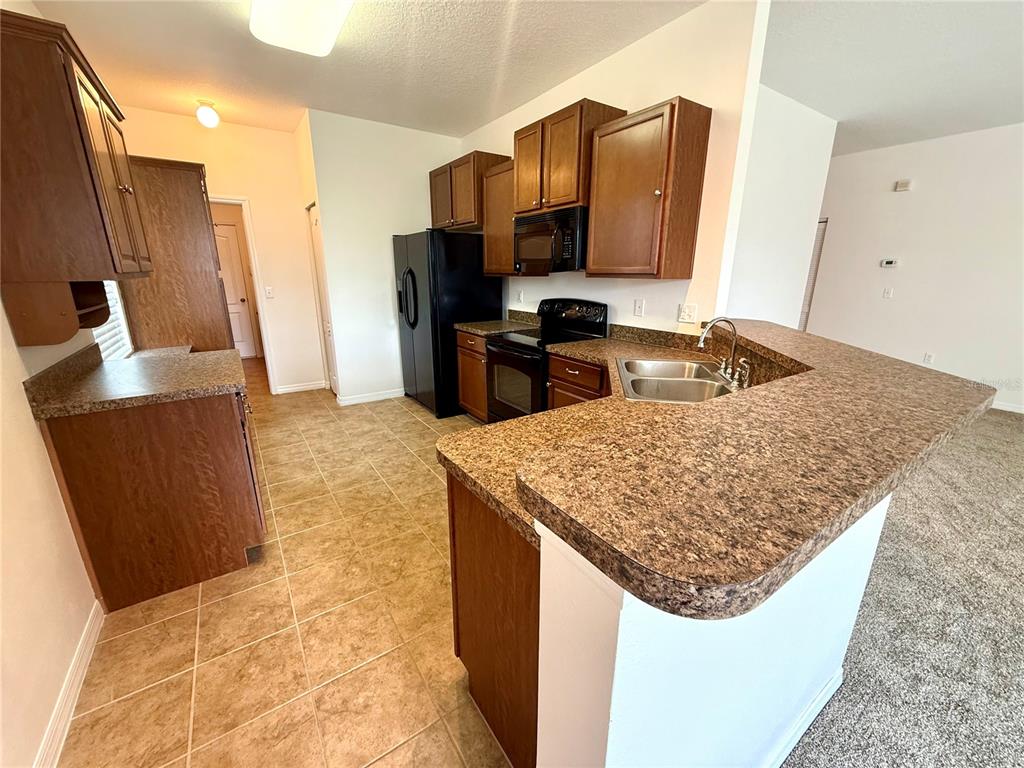 A kitchen features brown cabinets, laminate countertops, a black refrigerator, and a tile floor — 2616 WALDEN WOODS DRIVE, PLANT CITY, FL