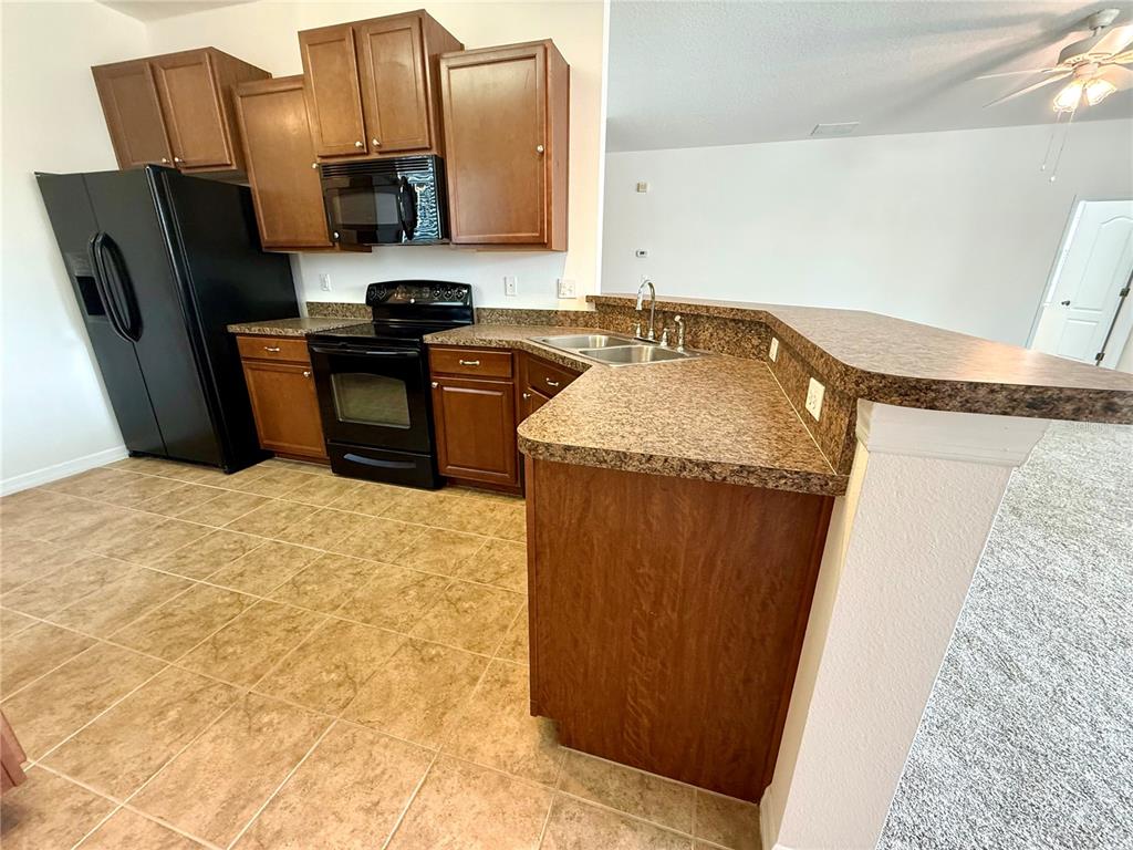 A kitchen features brown cabinets, black appliances, a laminate countertop, and tiled flooring — 2616 WALDEN WOODS DRIVE, PLANT CITY, FL