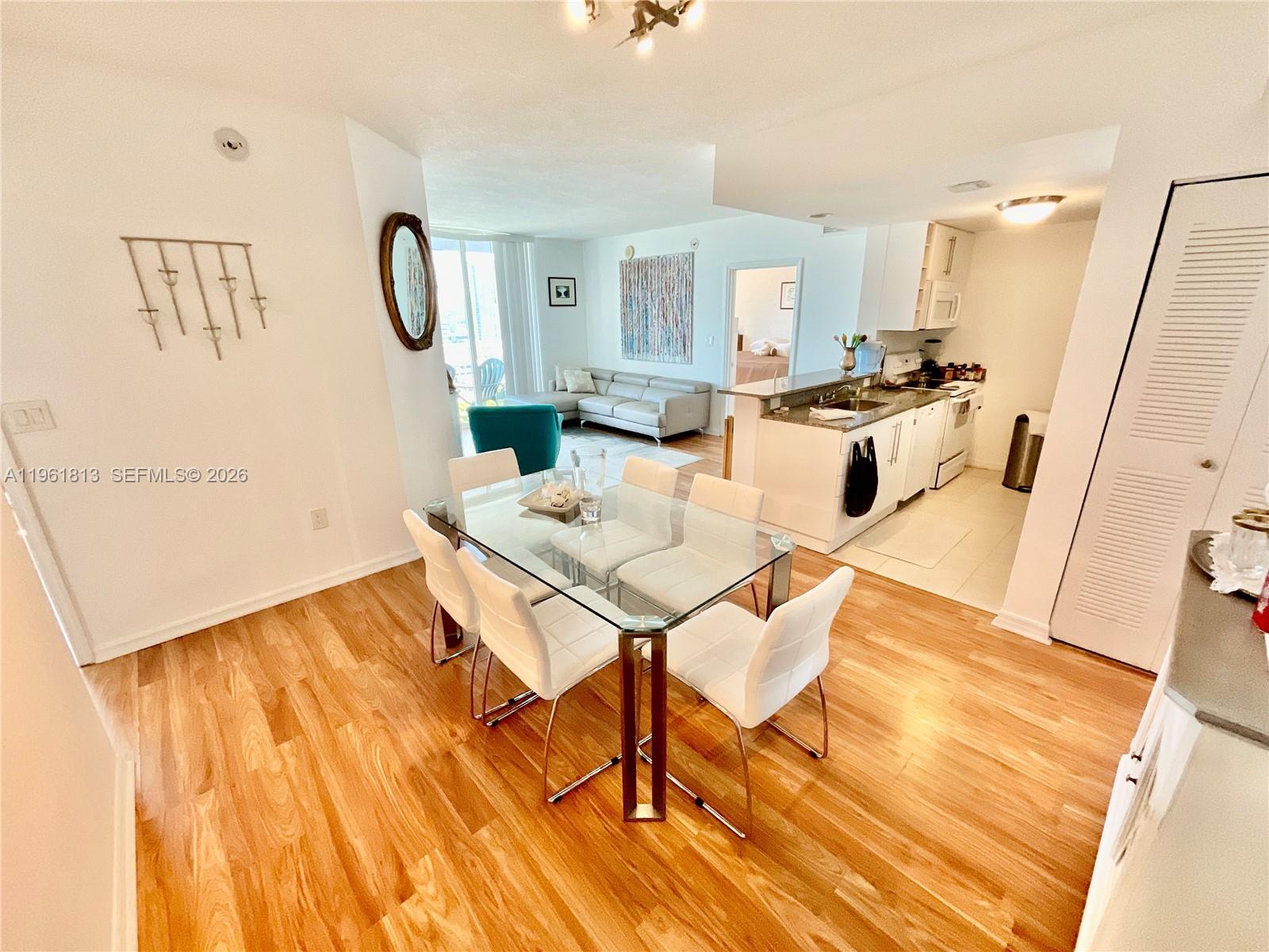 A dining area with a glass table and white chairs opens into a kitchen and living room — 275 NE 18th St # 1705, Miami FL 33132, MIAMI, FL