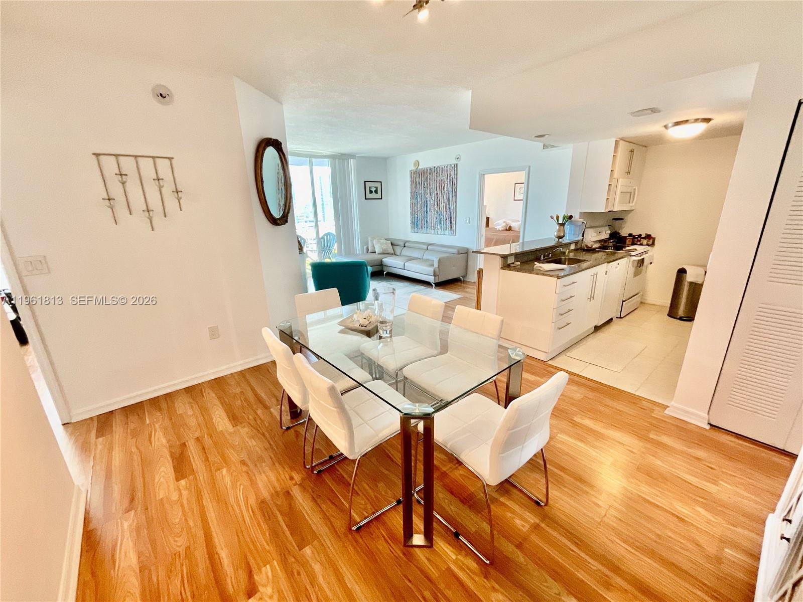 A dining area with a glass table and white chairs sits adjacent to a kitchen — 275 NE 18th St # 1705, Miami FL 33132, MIAMI, FL