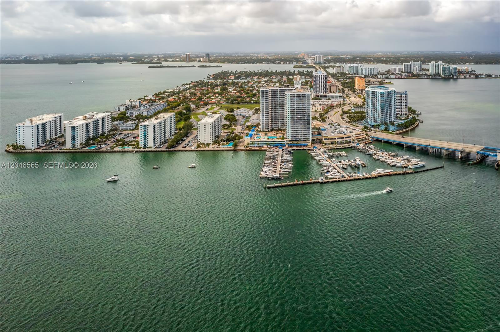 An aerial view shows a coastal neighborhood with high-rise apartment buildings, a marina, and a bridge — NORTH BAY VILLAGE, FL