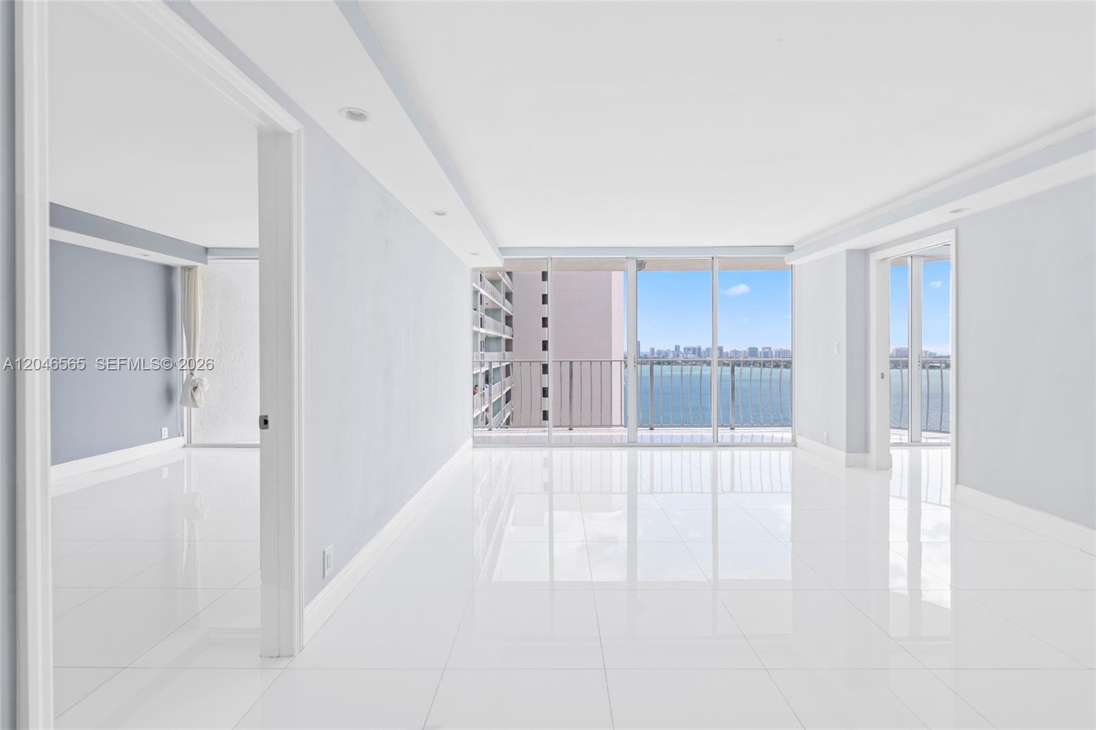 A bright, empty living area features white tile floors, recessed lighting, and floor-to-ceiling balcony windows — NORTH BAY VILLAGE, FL