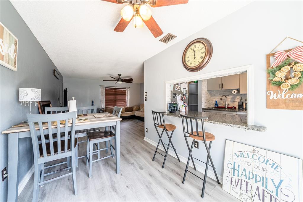 A dining area and kitchen pass-through with bar seating, gray wood-look flooring, and light walls — 2410 SE 16TH AVENUE UNIT F, OCALA, FL