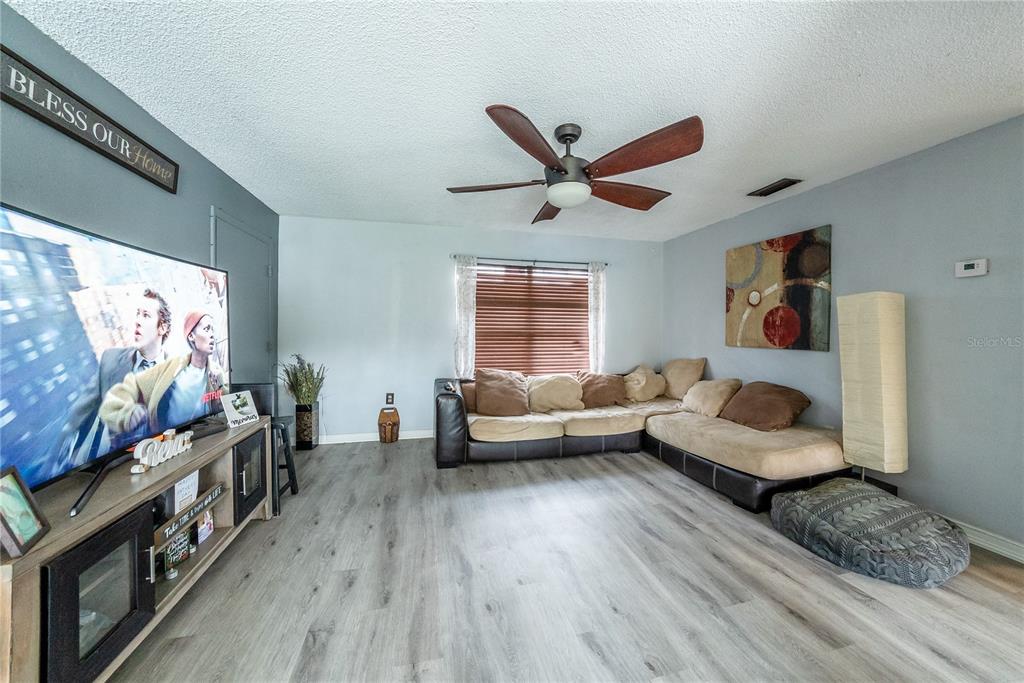A living room features light gray walls, wood-look flooring, a sectional sofa, and a television — 2410 SE 16TH AVENUE UNIT F, OCALA, FL