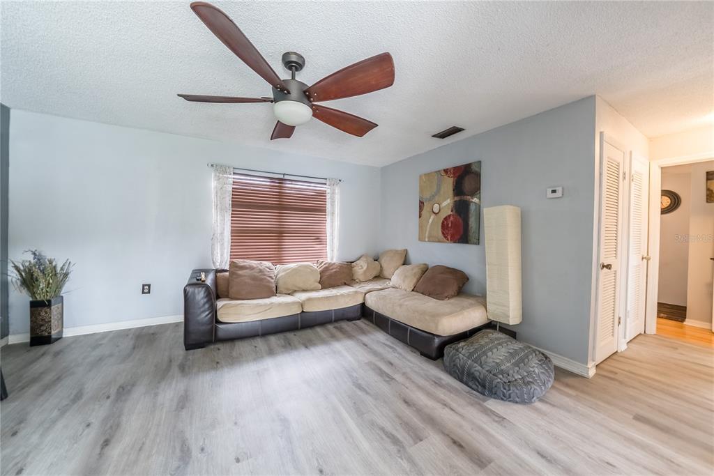 A living room features light gray walls, wood-look flooring, a ceiling fan, and a sectional sofa — 2410 SE 16TH AVENUE UNIT F, OCALA, FL