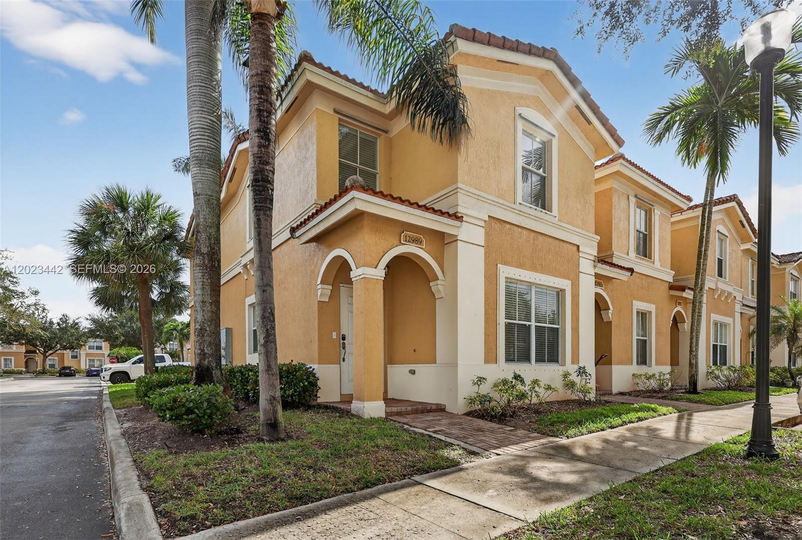 A two-story tan stucco townhouse features arched entryways, a tiled roof, and palm trees — 12989 SW 30th Ct # 135, Miramar FL 33027, MIRAMAR, FL