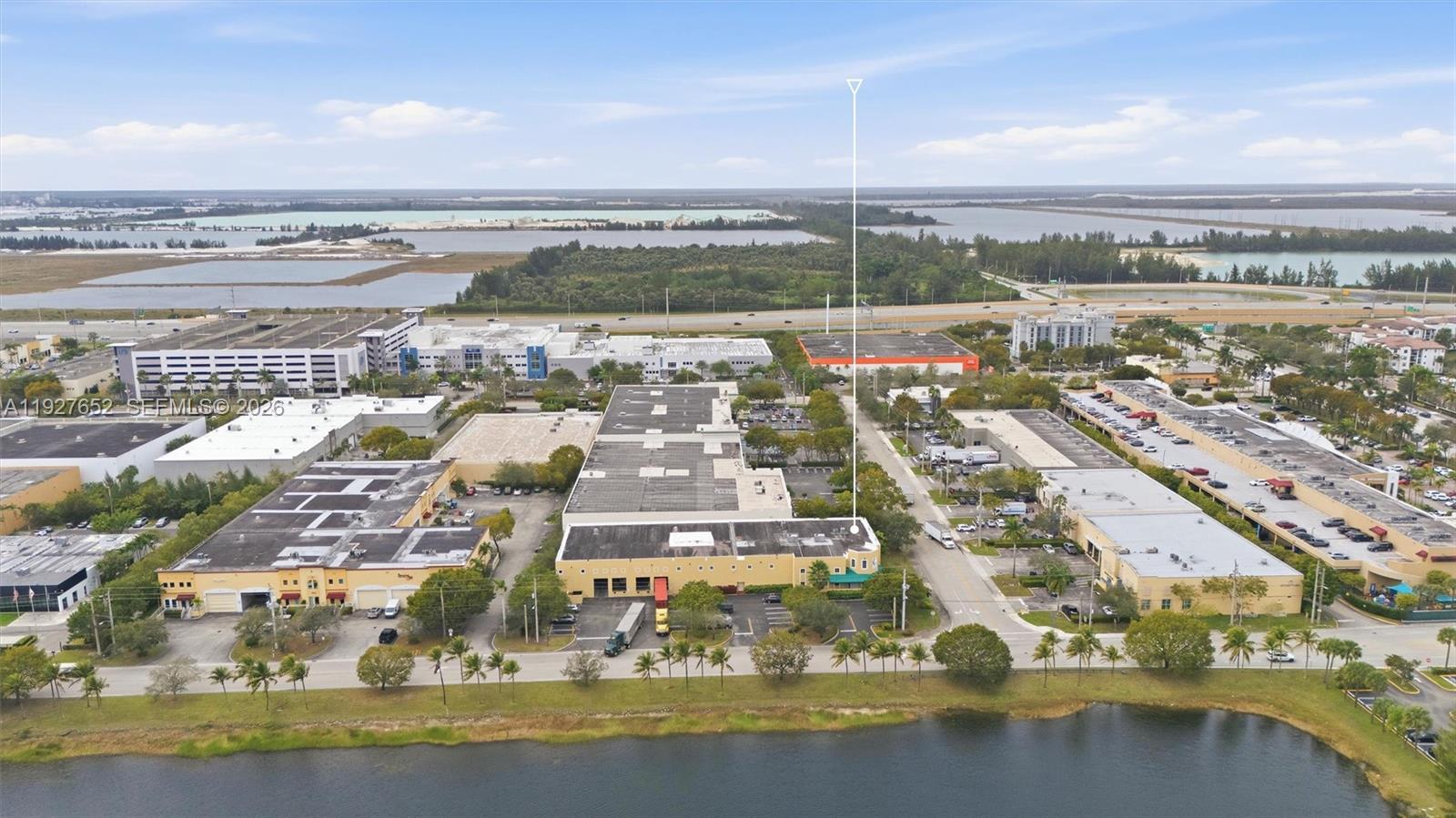 An aerial view shows a commercial building complex with parking lots and a nearby lake — 3850 NW 114th Ave, Doral FL 33178, DORAL, FL