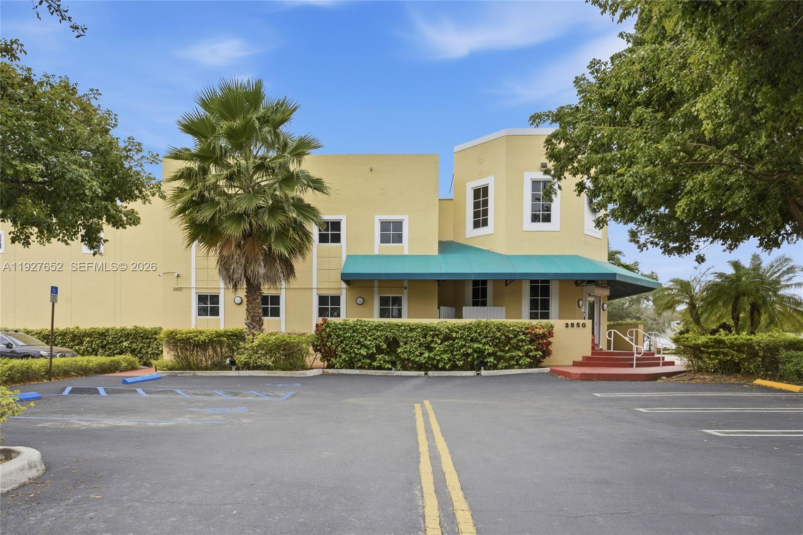 A two-story yellow commercial building features a green awning and a paved parking lot — 3850 NW 114th Ave, Doral FL 33178, DORAL, FL