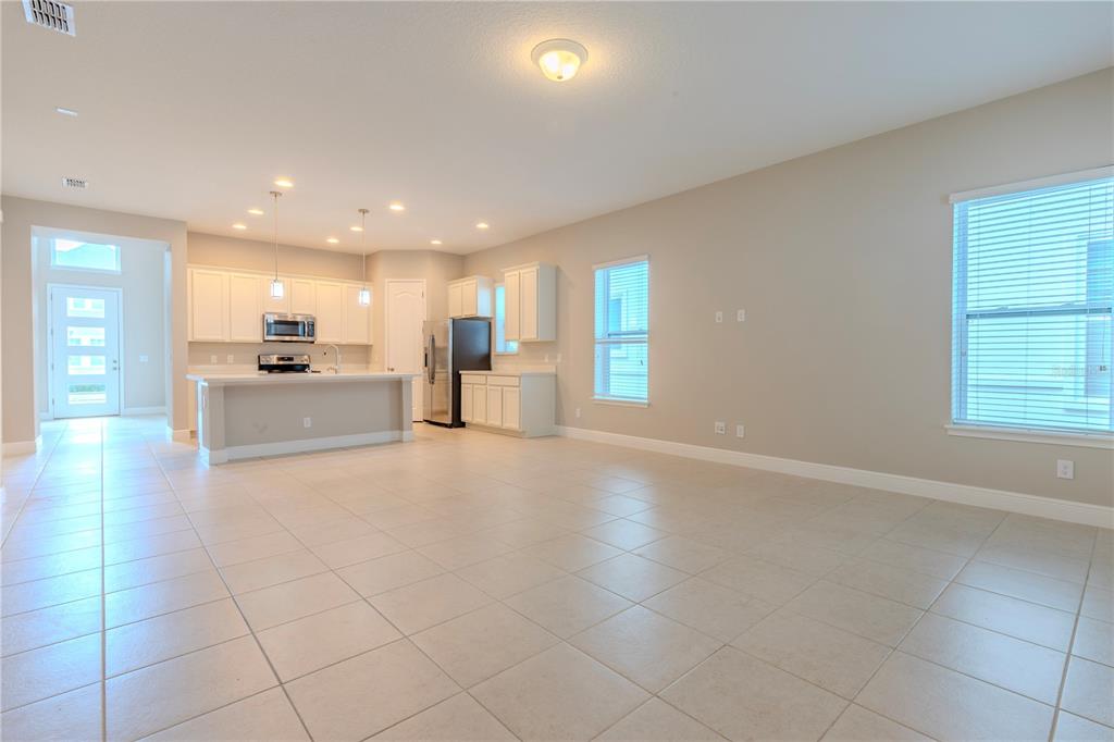 An open-concept kitchen and living area features light tile flooring, white cabinetry, and stainless appliances — 9233 SMITHIES STREET, ORLANDO, FL