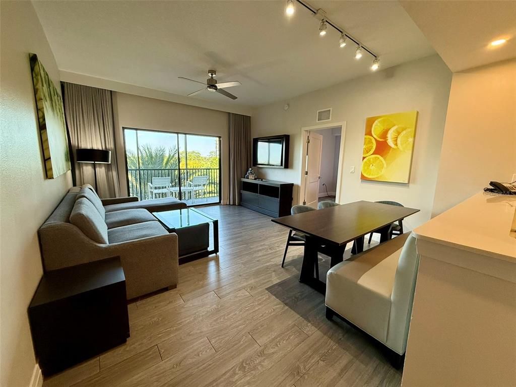 A living and dining area features wood-look flooring, a gray sofa, and a balcony view — 14501 GROVE RESORT AVE UNIT 2413, WINTER GARDEN, FL