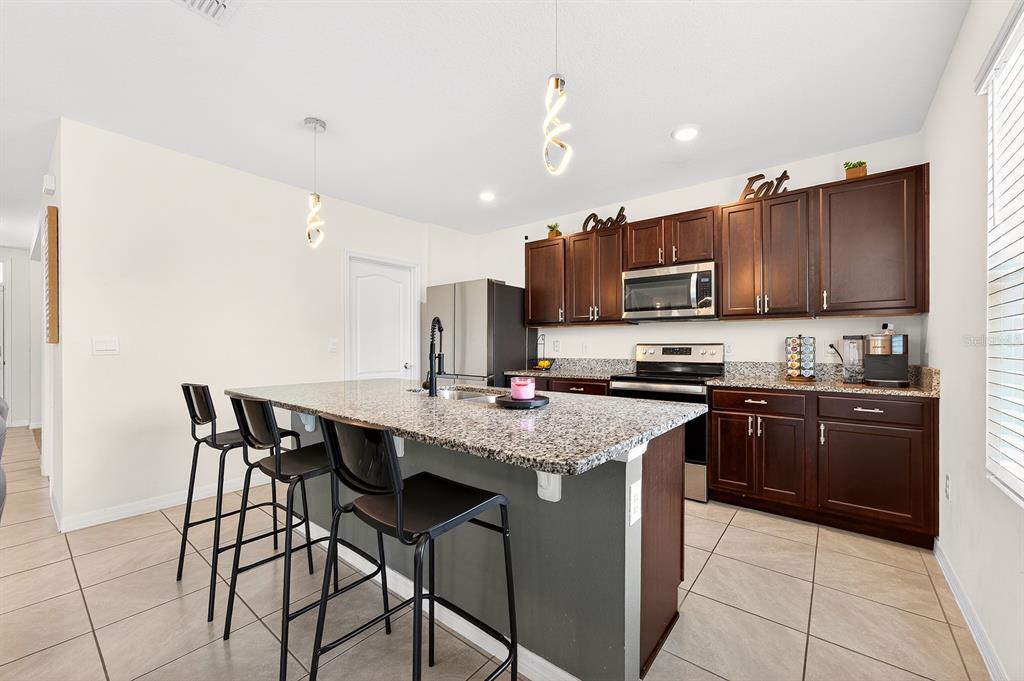 A kitchen features dark wood cabinets, granite countertops, a center island, and tile flooring — 3353 EASTGROVE TERRACE, SANFORD, FL
