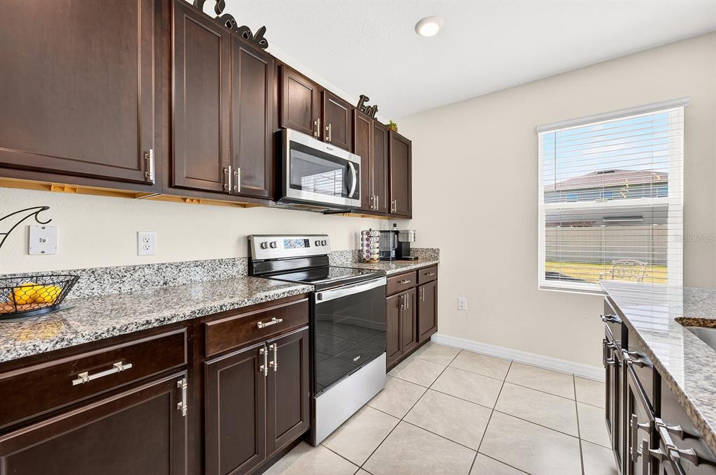 A kitchen features dark wood cabinets, granite countertops, stainless steel appliances, and tile flooring — 3353 EASTGROVE TERRACE, SANFORD, FL