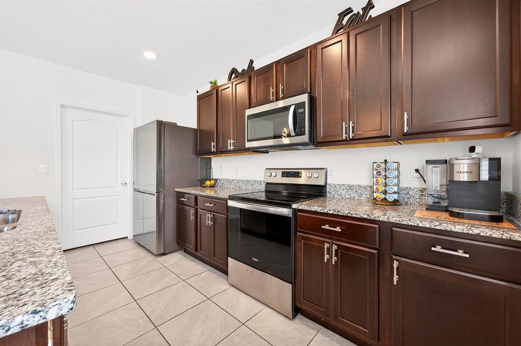 A kitchen features dark wood cabinets, granite countertops, stainless steel appliances, and tile flooring — 3353 EASTGROVE TERRACE, SANFORD, FL