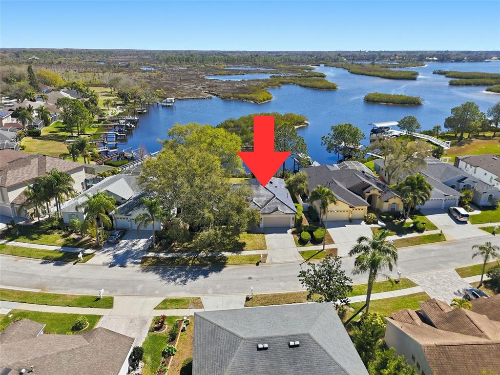 An aerial view shows a suburban house with a red arrow pointing toward its roof — 1857 RIVEREDGE DRIVE, TARPON SPRINGS, FL
