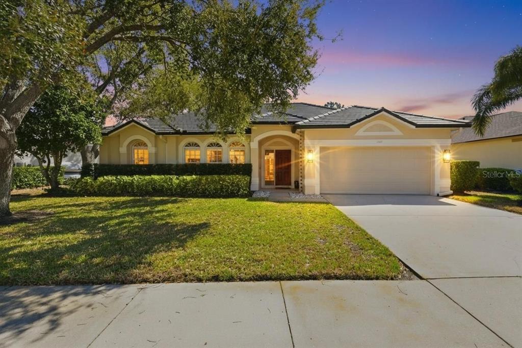 A single-story house with a two-car garage and a landscaped front yard at dusk — 1857 RIVEREDGE DRIVE, TARPON SPRINGS, FL