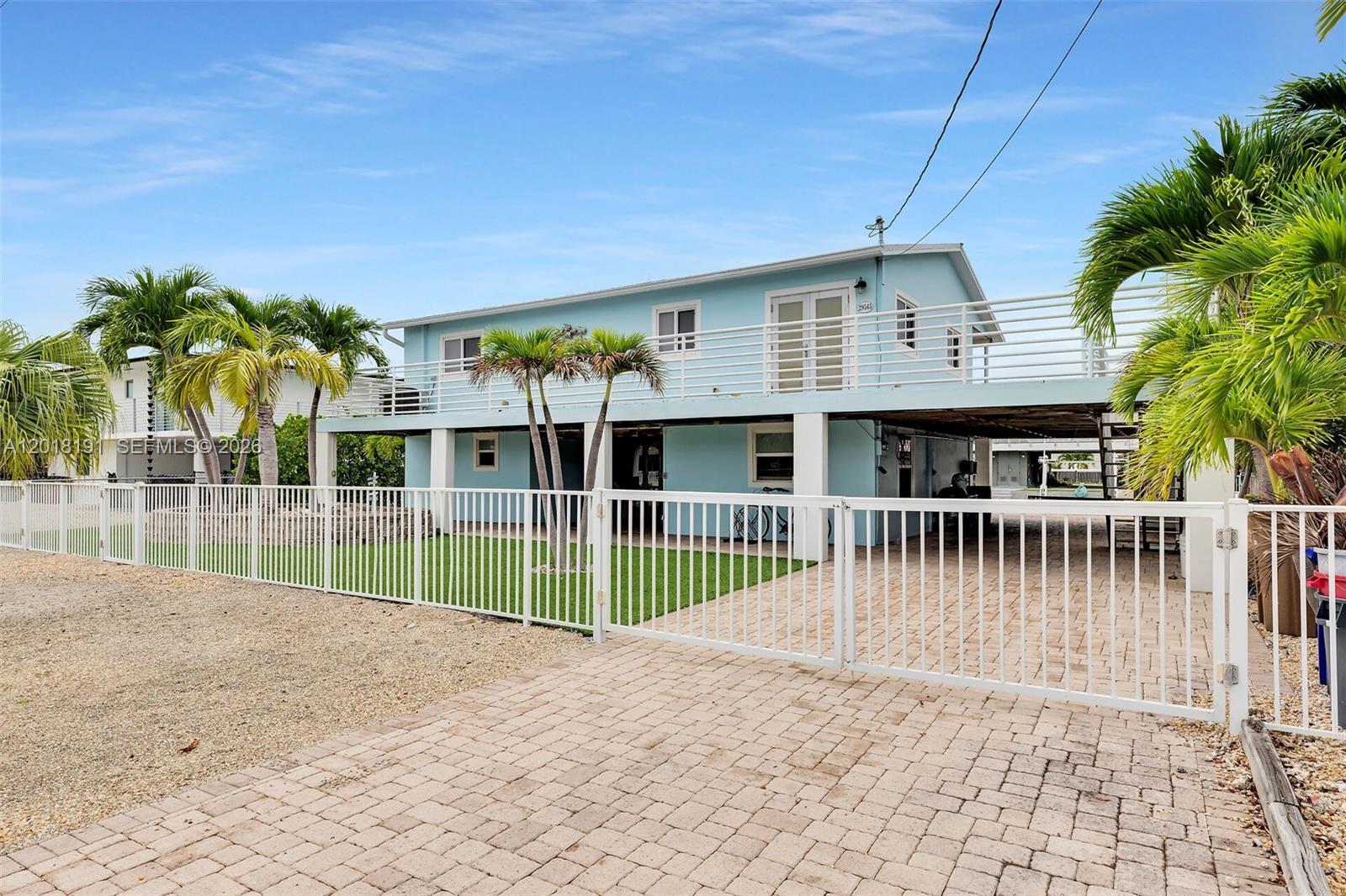 A light blue, elevated two-story house features a white fence and a paved driveway — 29565 Flying Cloud Ave, Big Pine FL 33043, BIG PINE, FL