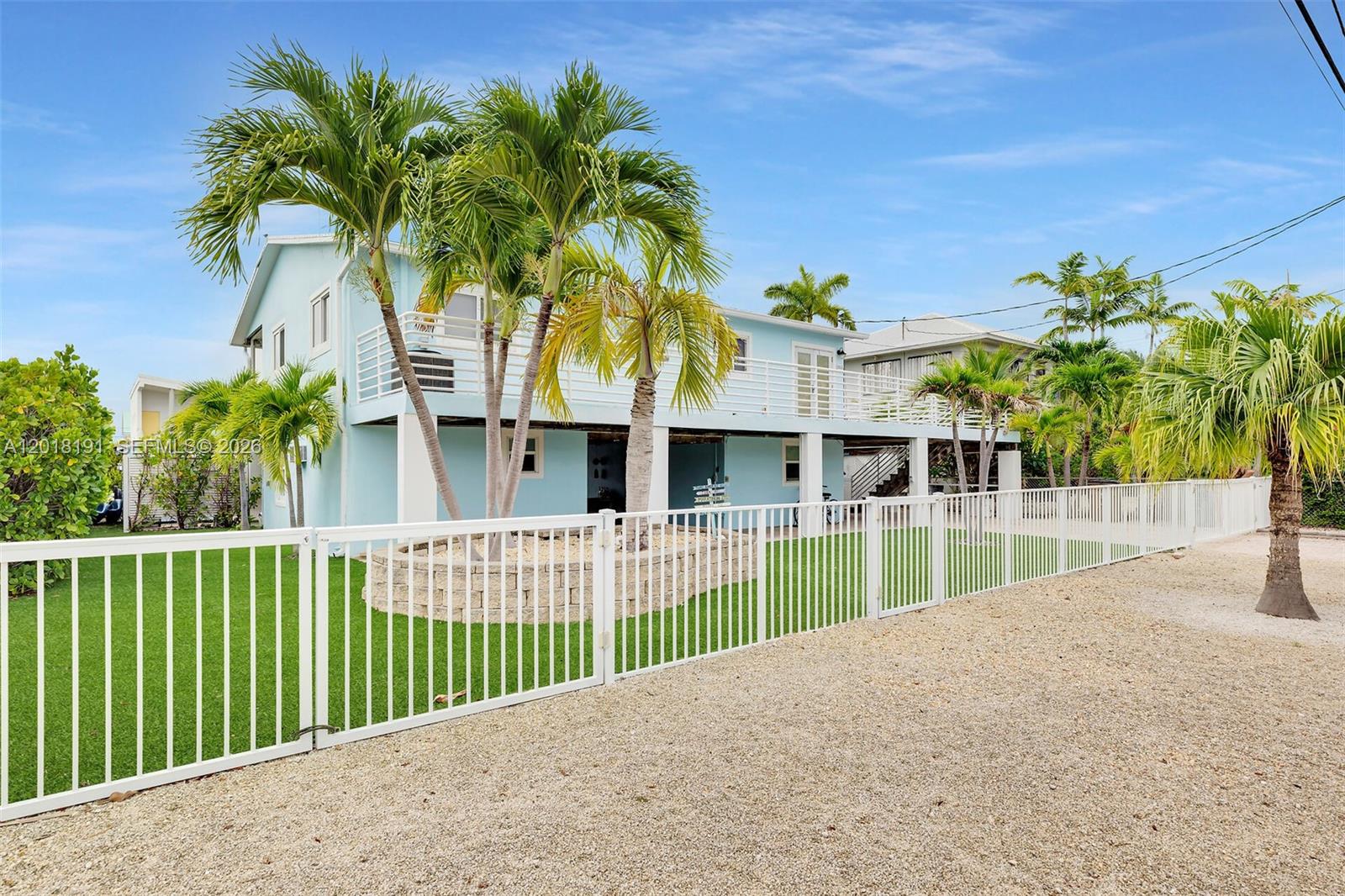 A light blue two-story house features a white fence, palm trees, and a gravel yard — 29565 Flying Cloud Ave, Big Pine FL 33043, BIG PINE, FL