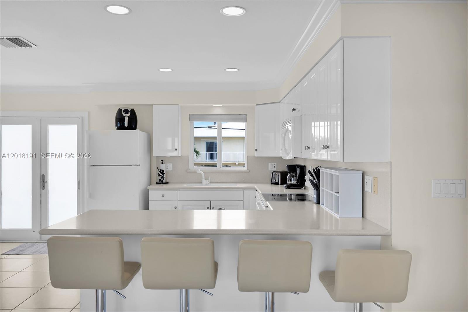 A modern kitchen features white cabinets, a breakfast bar with four stools, and recessed lighting — 29565 Flying Cloud Ave, Big Pine FL 33043, BIG PINE, FL