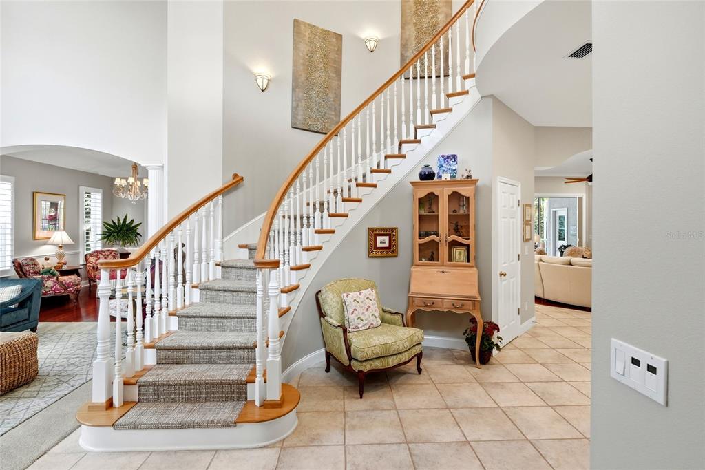 A grand foyer features a curved staircase with a carpet runner and a light-colored tile floor — 1246 DARLINGTON OAK CIRCLE NE, ST PETERSBURG, FL