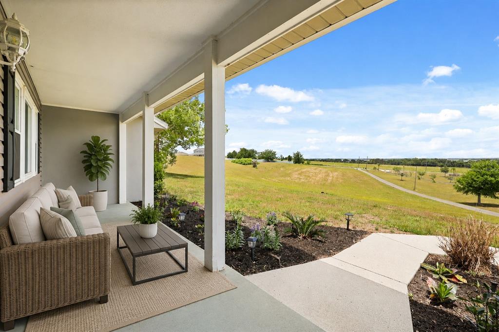A covered porch with outdoor seating overlooks a grassy field under a blue sky — 37153 COUNTY ROAD 452, GRAND ISLAND, FL