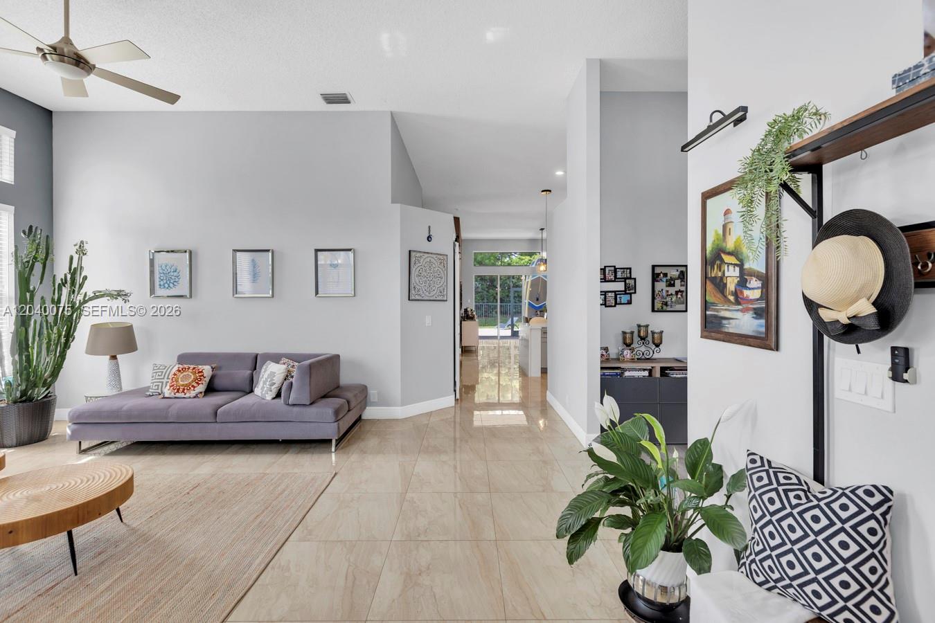 A bright living room features light tile floors, a gray sofa, and a tall cactus — 19700 Dinner Key Dr, Boca Raton FL 33498, BOCA RATON, FL
