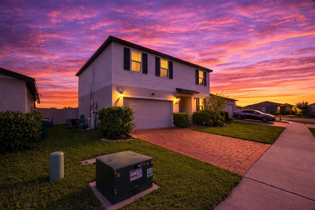 A two-story house with a brick driveway and a sunset sky in the background — 441 MCKENNA DRIVE, WINTER HAVEN, FL
