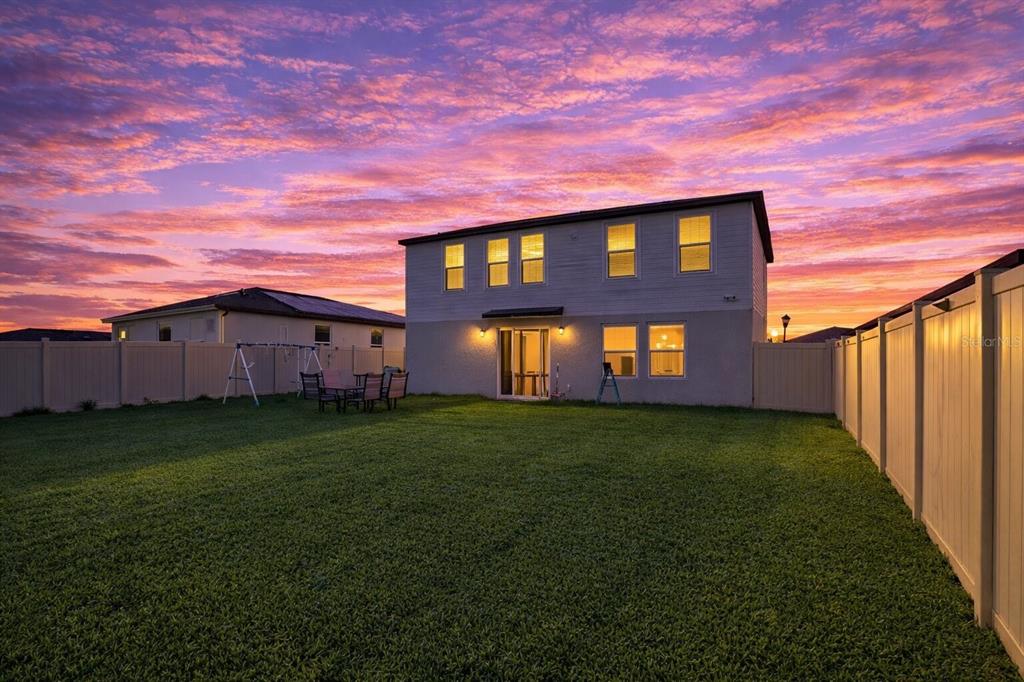 The backyard of a two-story house features a grassy lawn and a white vinyl fence — 441 MCKENNA DRIVE, WINTER HAVEN, FL