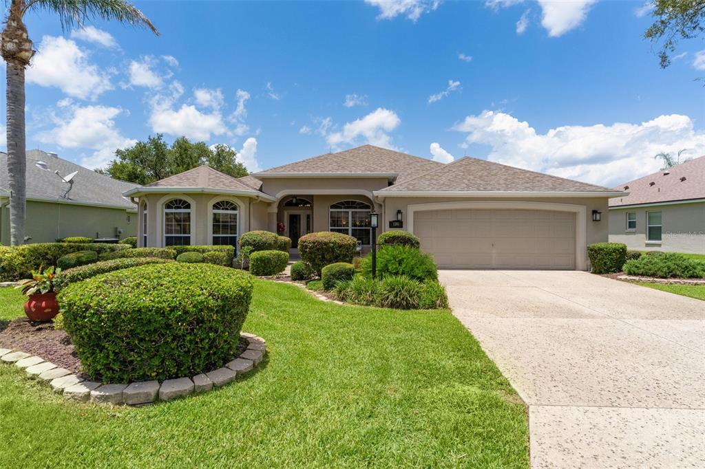 A single-story suburban house with a two-car garage, manicured landscaping, and a sunset sky — 1281 BETHUNE WAY, THE VILLAGES, FL