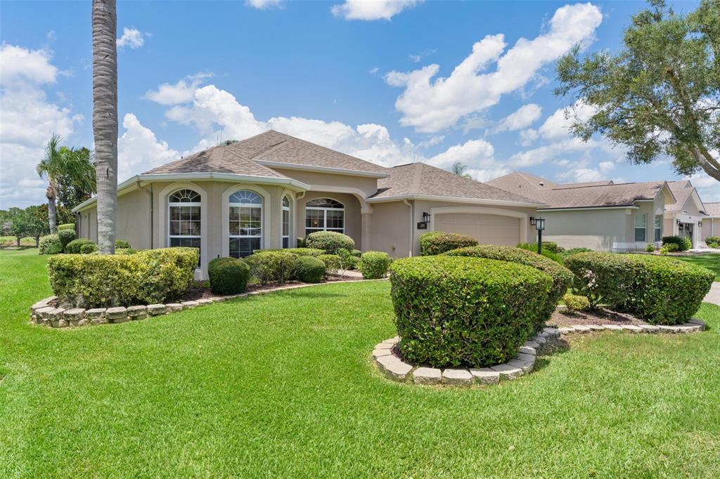 A single-story house with a beige stucco exterior, a two-car garage, and a landscaped lawn — 1281 BETHUNE WAY, THE VILLAGES, FL
