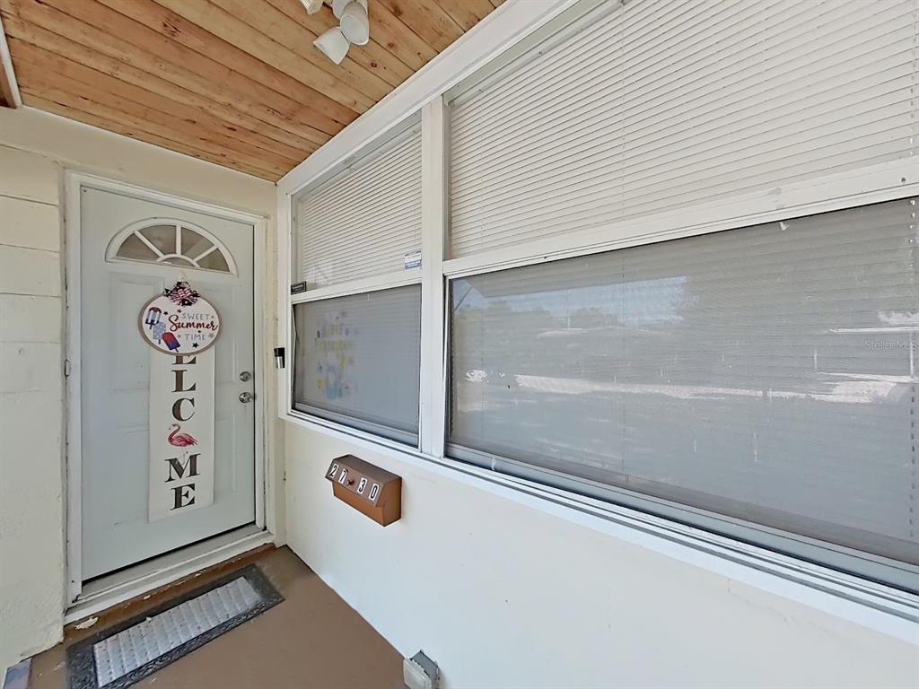 A covered porch features a white front door, large windows with blinds, and wood-paneled ceiling — 2730 EDWARDS AVENUE S, ST PETERSBURG, FL