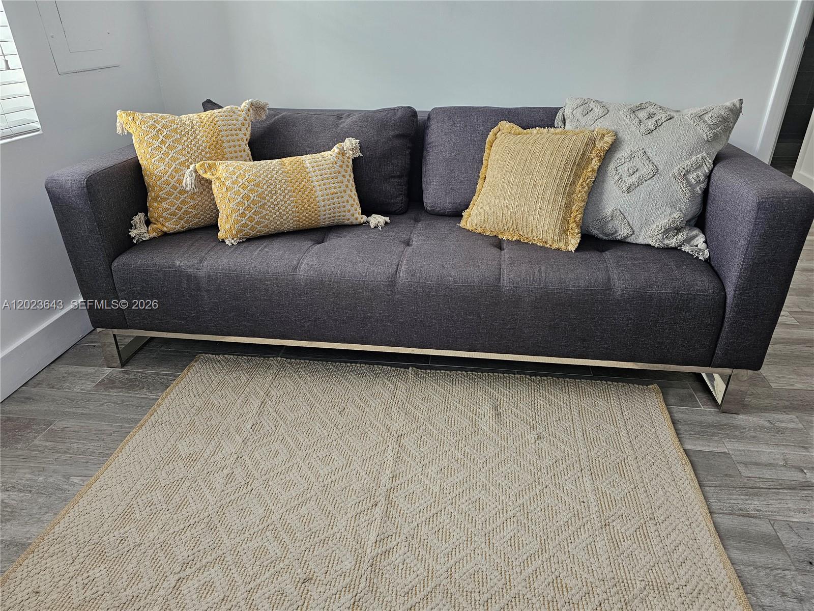 A gray sofa with yellow and textured pillows sits on a rug in a room — 622 15th St # 6, Miami Beach FL 33139, MIAMI BEACH, FL