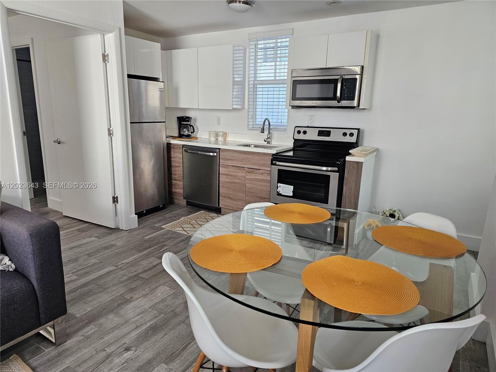 A kitchen with stainless steel appliances and wood-toned cabinets sits next to a dining area — 622 15th St # 6, Miami Beach FL 33139, MIAMI BEACH, FL