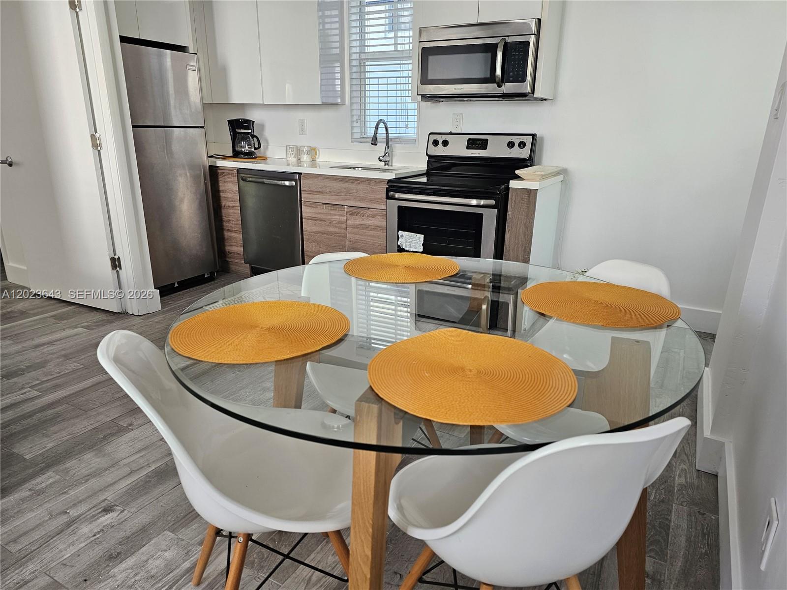 A kitchen with stainless steel appliances, wood-tone cabinets, and a glass-topped dining table — 622 15th St # 6, Miami Beach FL 33139, MIAMI BEACH, FL