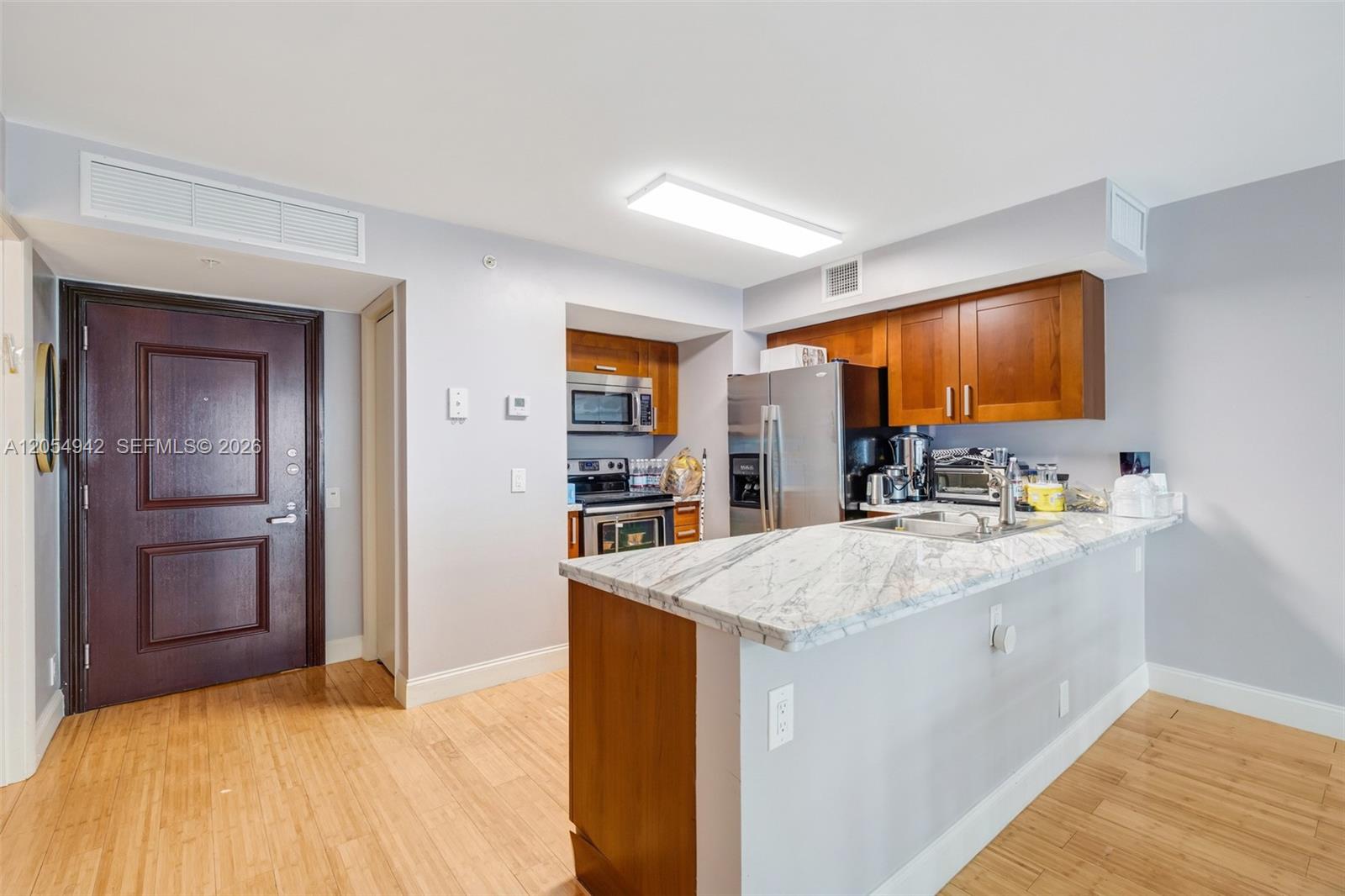 A kitchen features wood cabinets, stainless steel appliances, and a marble-topped breakfast bar — 9499 Collins Ave # 607, Surfside FL 33154, SURFSIDE, FL