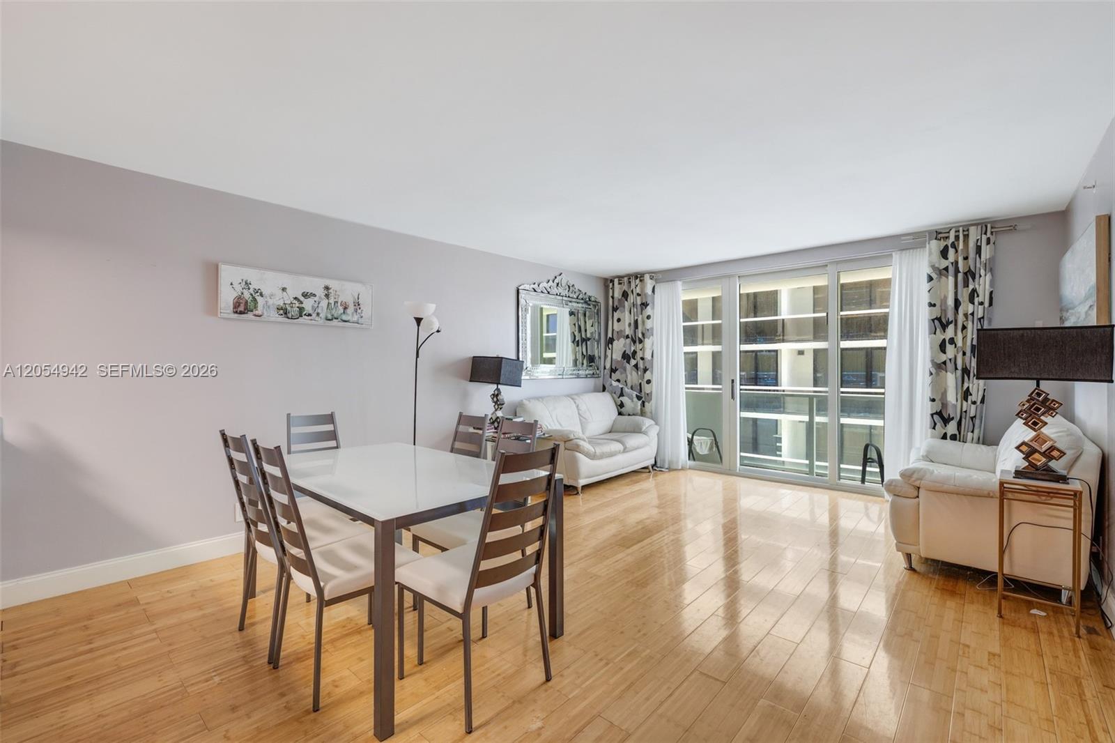A dining area and living space feature light wood flooring and a sliding glass door — 9499 Collins Ave # 607, Surfside FL 33154, SURFSIDE, FL