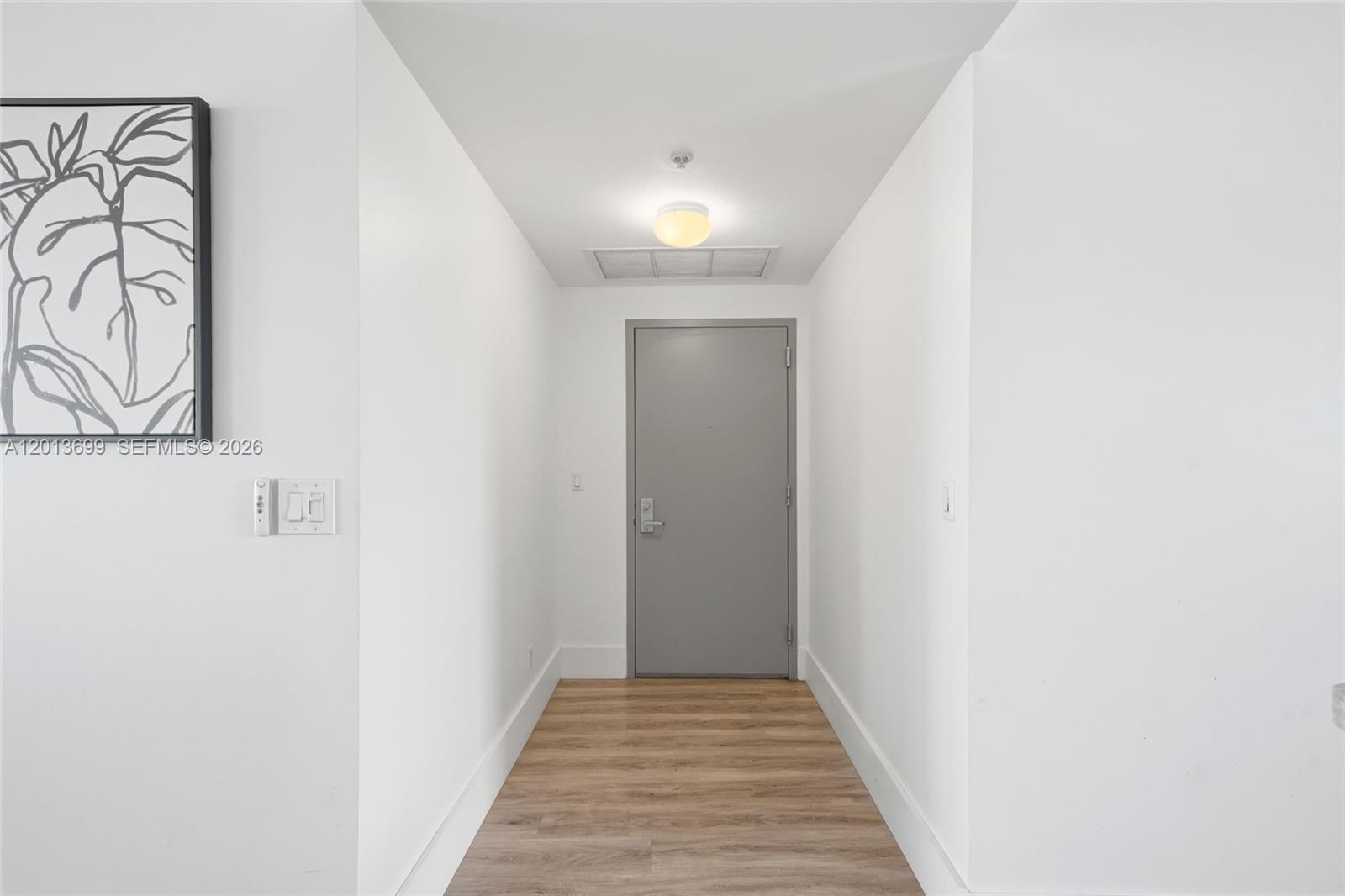 A hallway features white walls, light wood flooring, a gray door, and a framed print — 601 NE 36th St # 2707, Miami FL 33137, MIAMI, FL