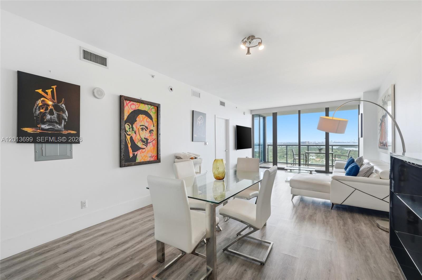 A modern dining and living area features a glass table, white chairs, and floor-to-ceiling windows — 601 NE 36th St # 2707, Miami FL 33137, MIAMI, FL