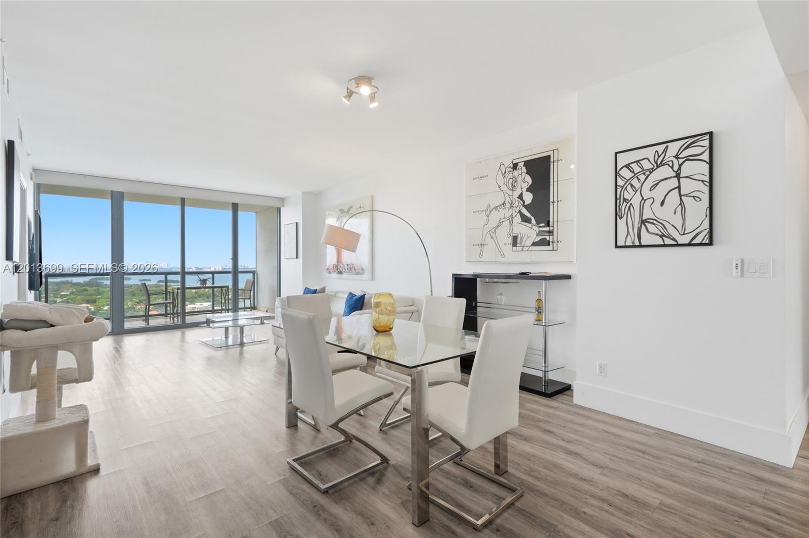 A modern dining area with a glass table, white chairs, and a balcony with water views — 601 NE 36th St # 2707, Miami FL 33137, MIAMI, FL