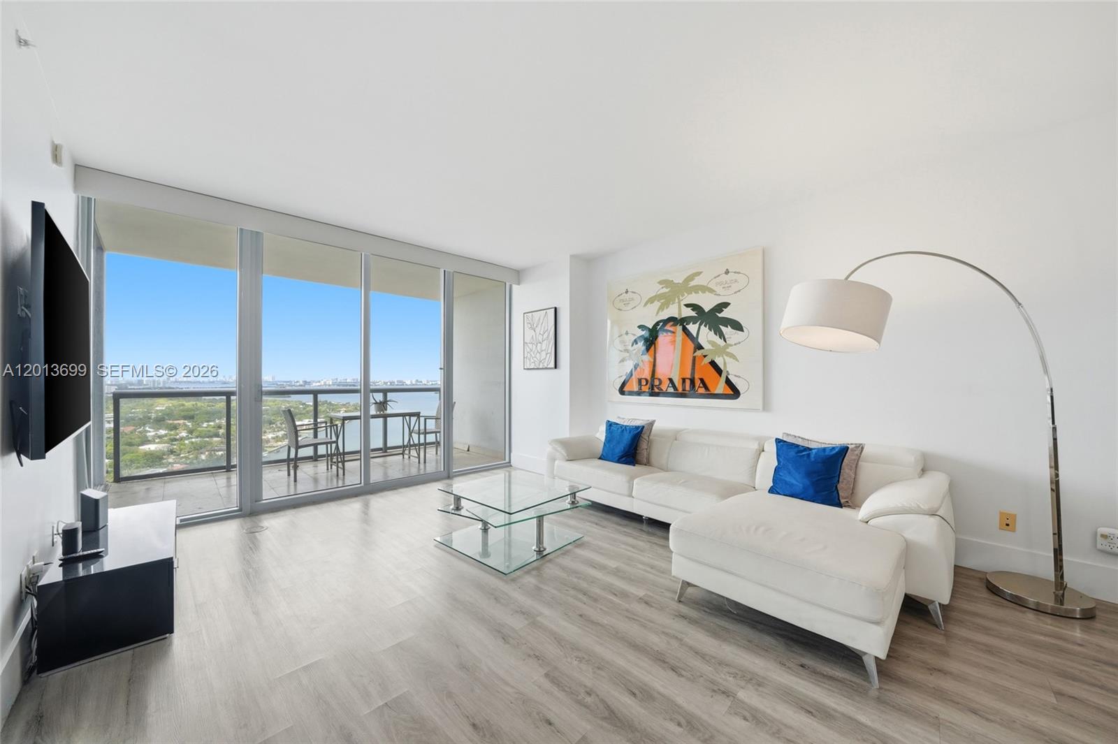 A bright living room features a white sectional sofa, glass coffee table, and balcony access — 601 NE 36th St # 2707, Miami FL 33137, MIAMI, FL