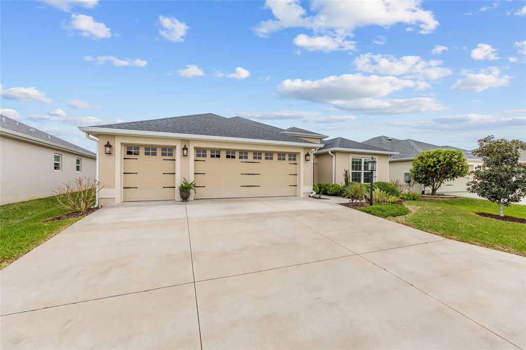 A single-story house with a three-car garage, beige stucco exterior, and a concrete driveway — 5791 HENRY LOOP, THE VILLAGES, FL