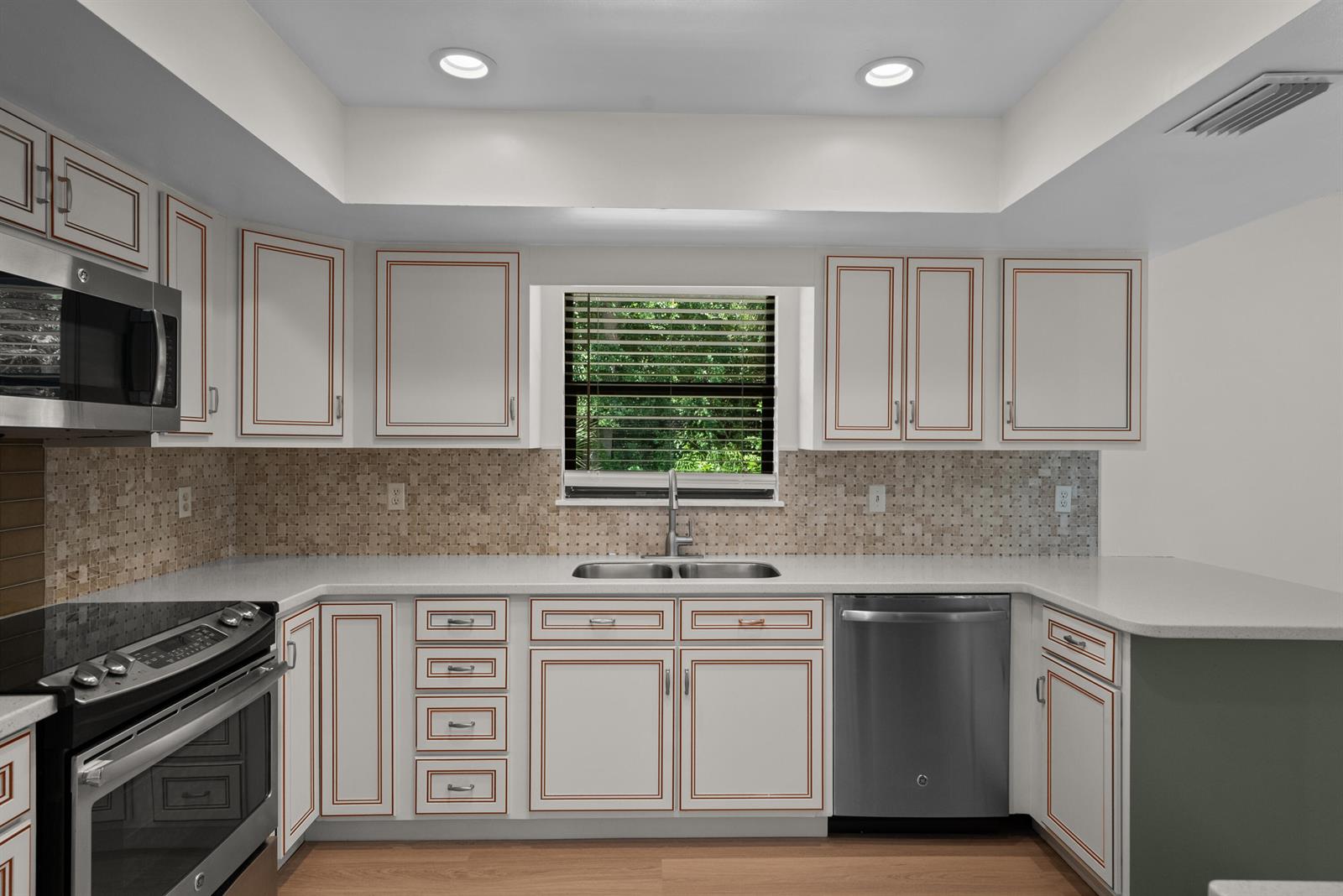 A kitchen features white cabinets with copper trim, stainless steel appliances, and a tiled backsplash — 700 NW North River Drive, Stuart FL 34994, STUART, FL