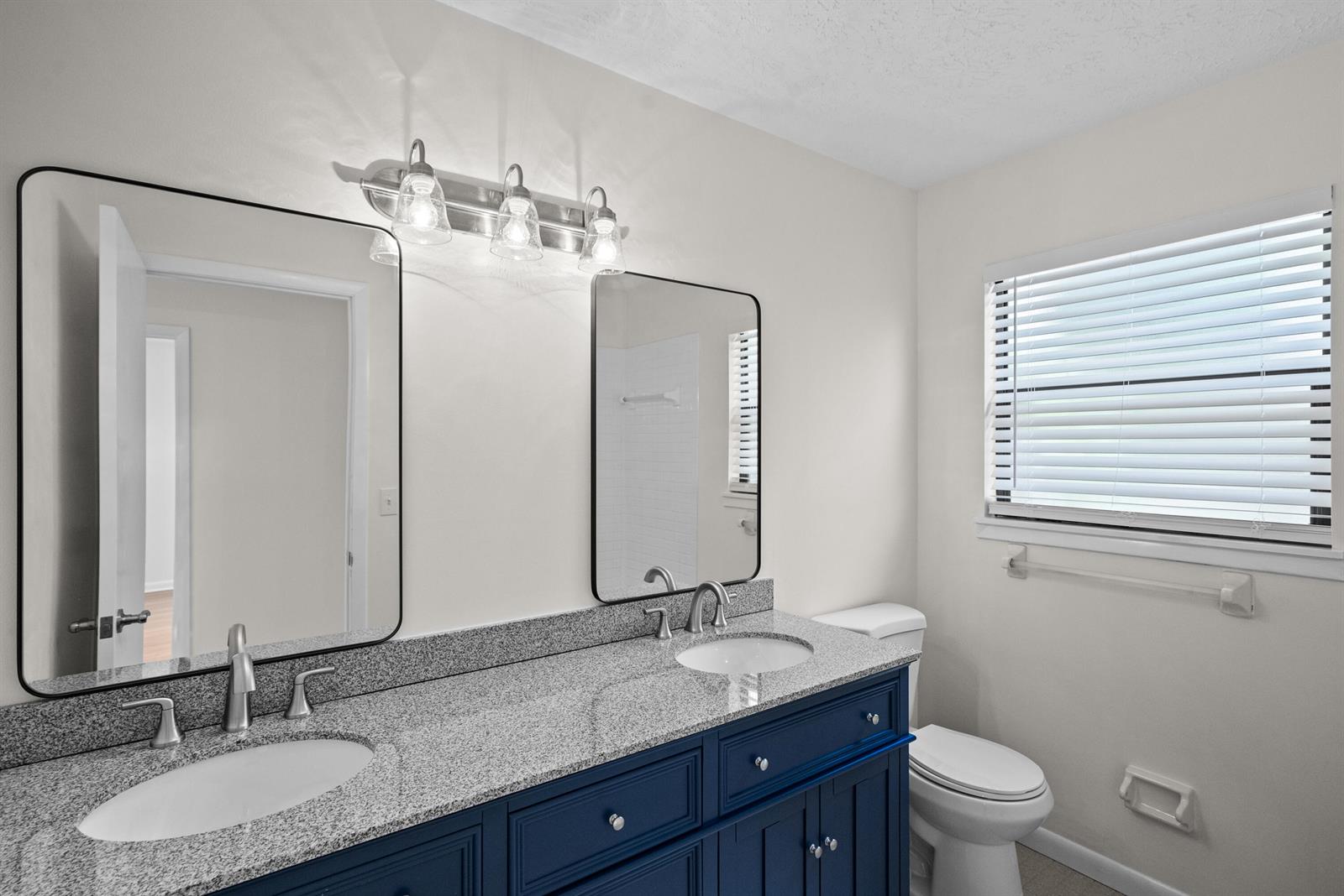A bathroom features a blue double vanity with granite countertops, two mirrors, and a toilet — 700 NW North River Drive, Stuart FL 34994, STUART, FL