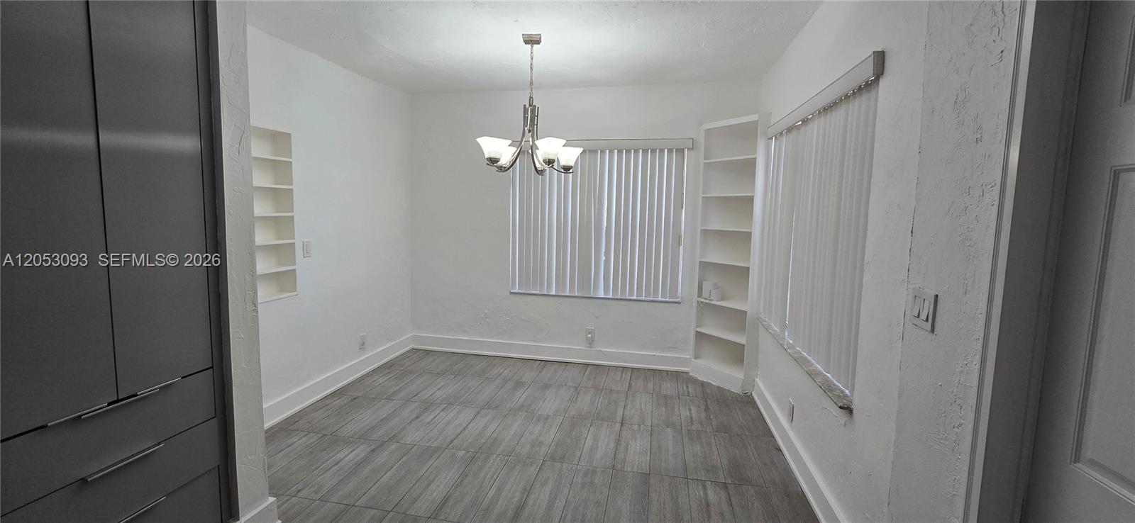 A dining room features gray wood-look tile flooring, white walls, built-in shelving, and a chandelier — 455 NE 131st St # 1, North Miami FL 33161, NORTH MIAMI, FL